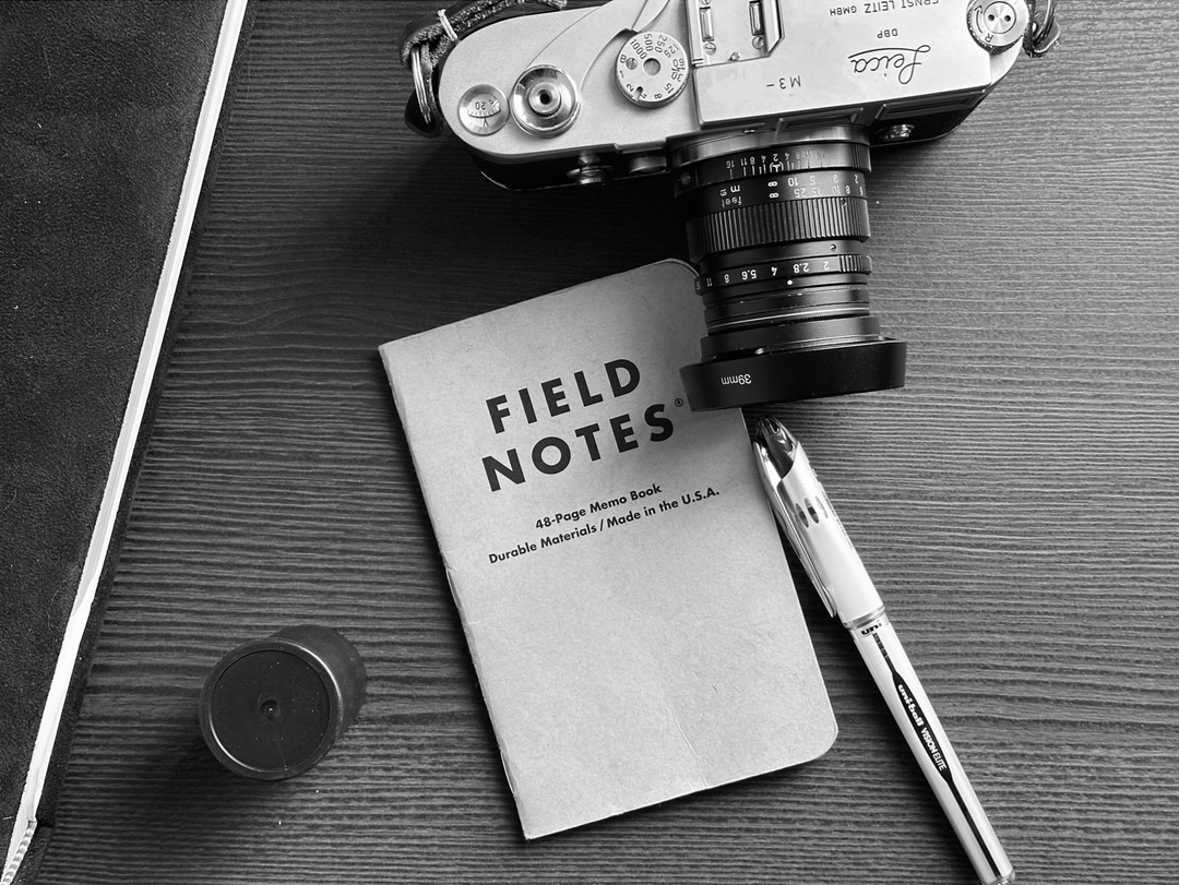 a vintage camera, a pen, a notebook & film canister in black & white