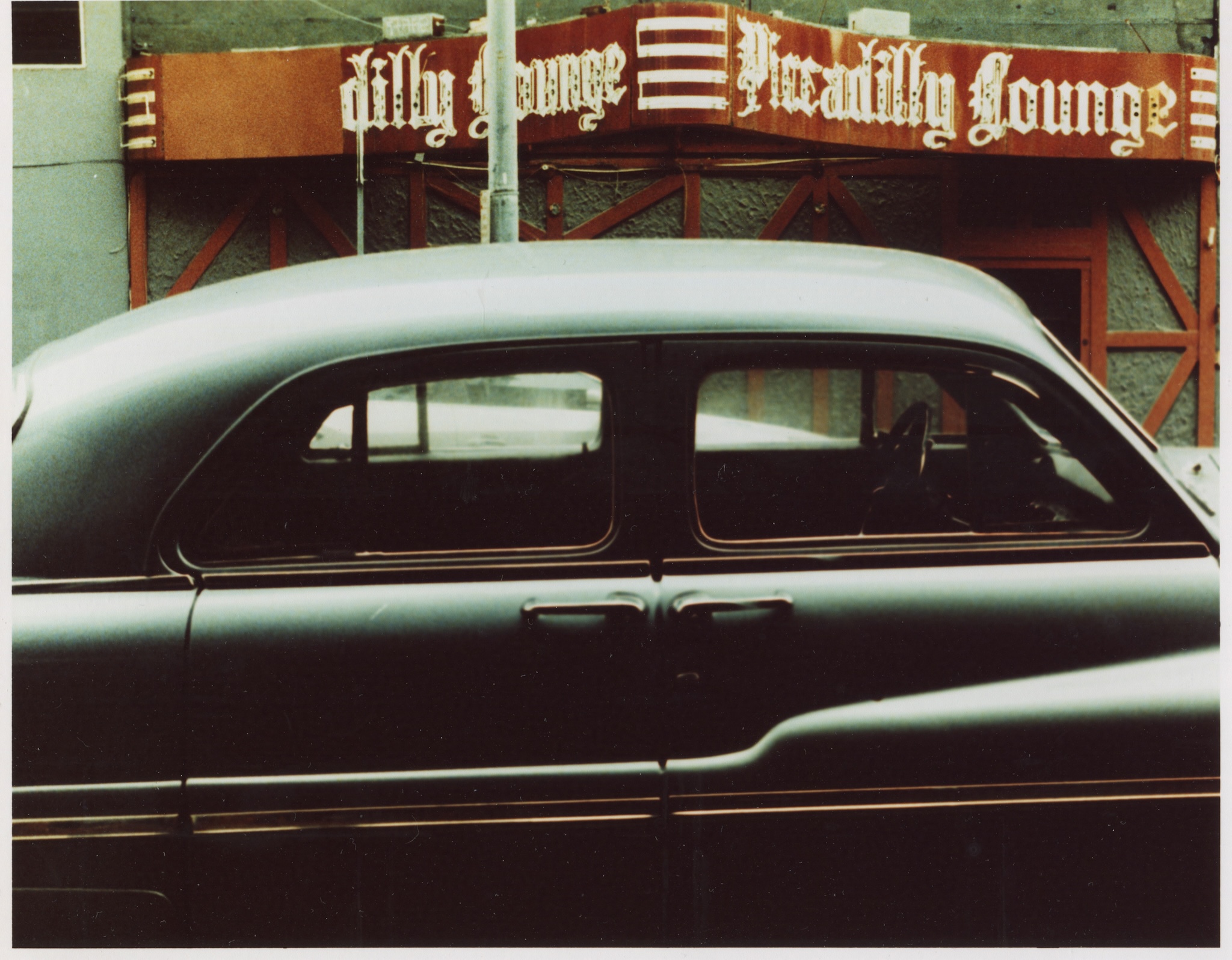 A muted color, grainy image of the top of a classic car with vintage marquee in the background