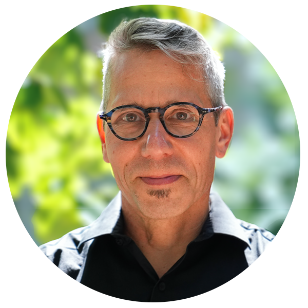 Image of Mika standing in dappled sunlight. Mika wears rounded glasses and is looking intently into the camera.